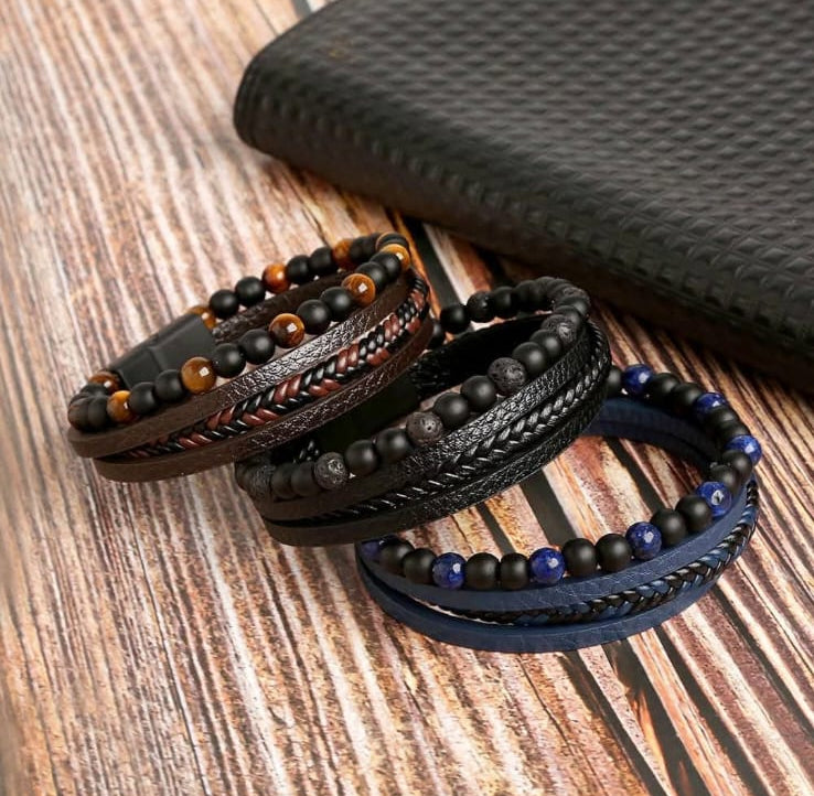 Three black leather wrap bracelets with beads and braided details, displayed on a wooden surface next to a black textured pouch.